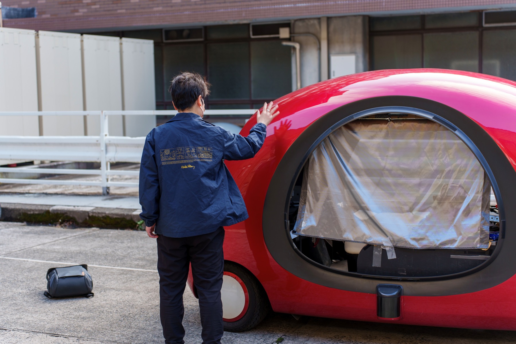 A person taps the exterior of the red autonomous vehicle used in the Tap2Stop project.